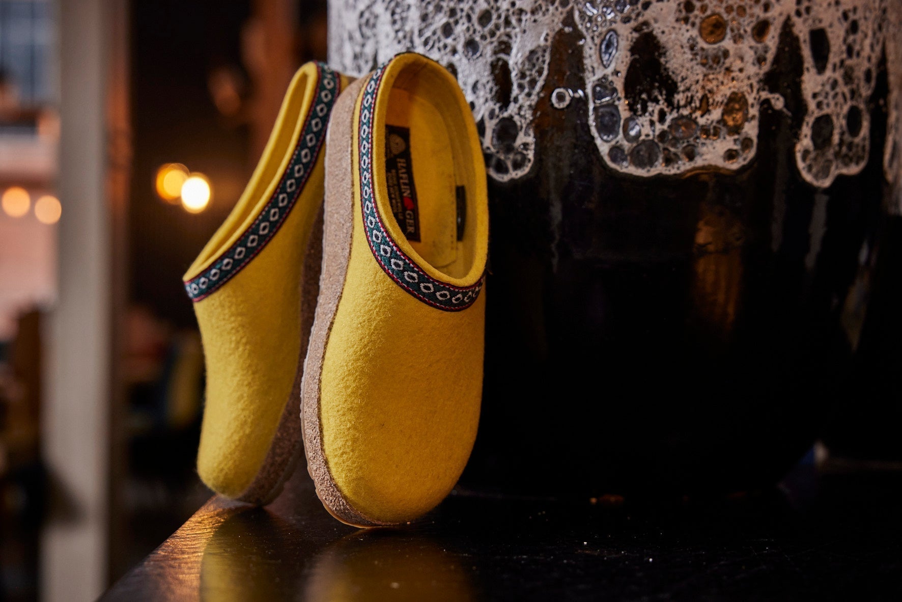 Pantofole Haflinger Franzl Sabot in feltro di lana vergine gialla su superficie nera con sfondo sfocato.