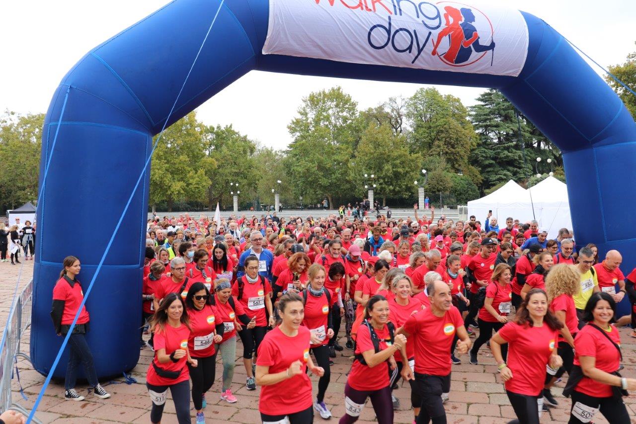 Gruppo di persone in maglietta rossa durante il Walking Day a Milano, evento di camminata all'aperto con arco blu con scritta "Walking Day".