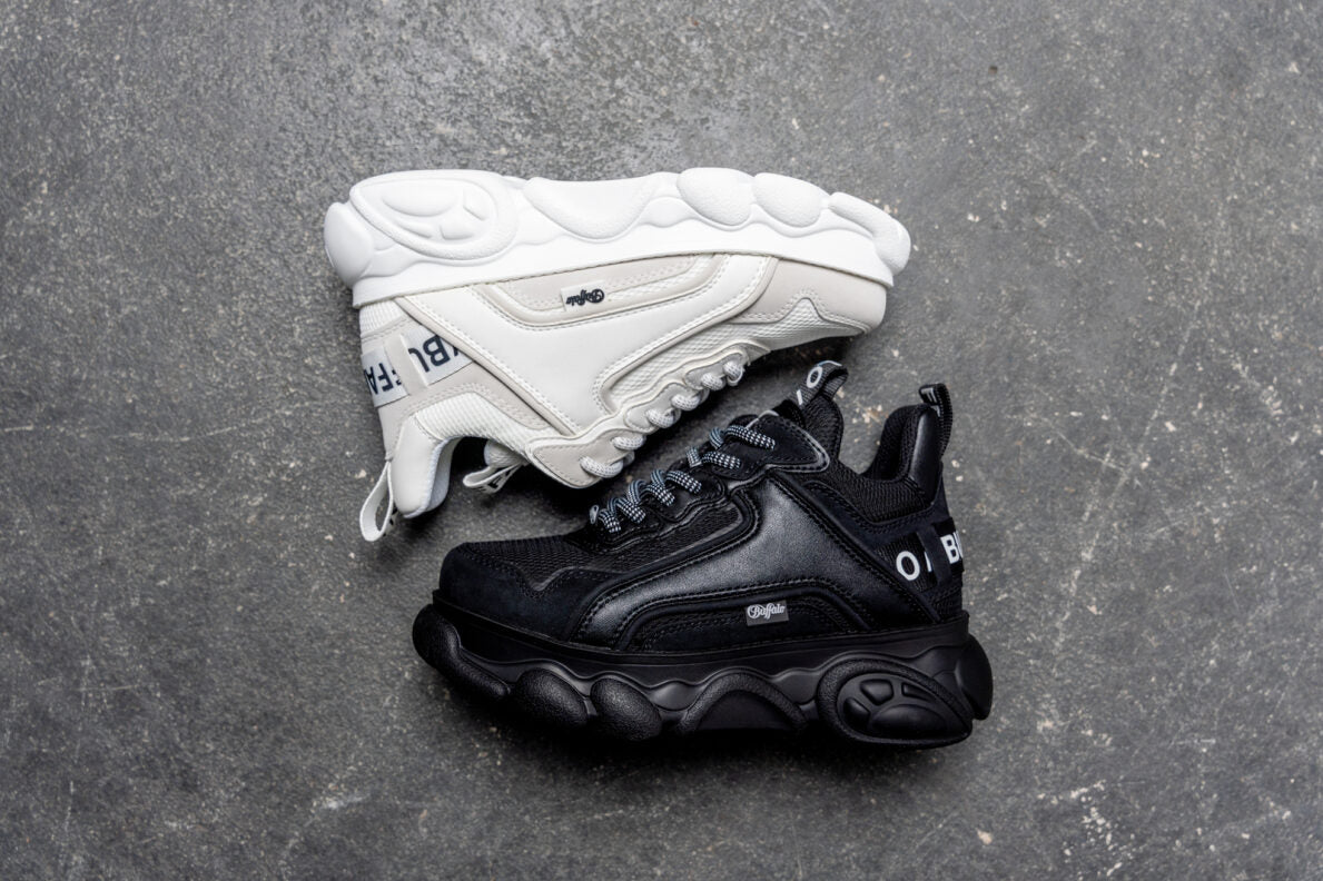 Sneaker chunky Buffalo Cld Chai, una bianca e una nera, in pelle vegana e mesh su sfondo in pietra grigia.