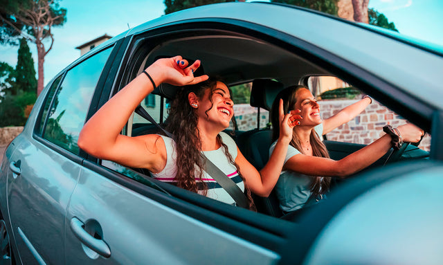 Due ragazze sorridenti in auto mentre si godono un viaggio estivo.
