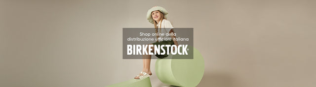bambina seduta su cilindro verde che indossa ciabatte birkenstock arizona kids electric metallic pearl