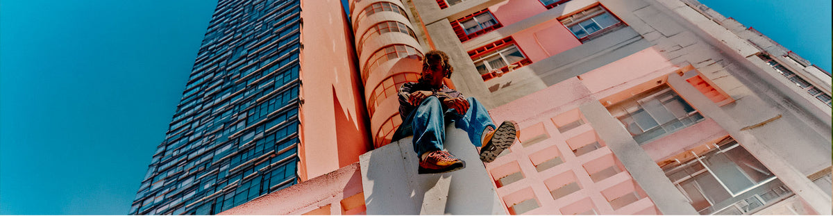 Scarpe KEEN Jasper indossate da una persona seduta su una struttura architettonica rosa in città, modello approach tra outdoor e quotidianità.