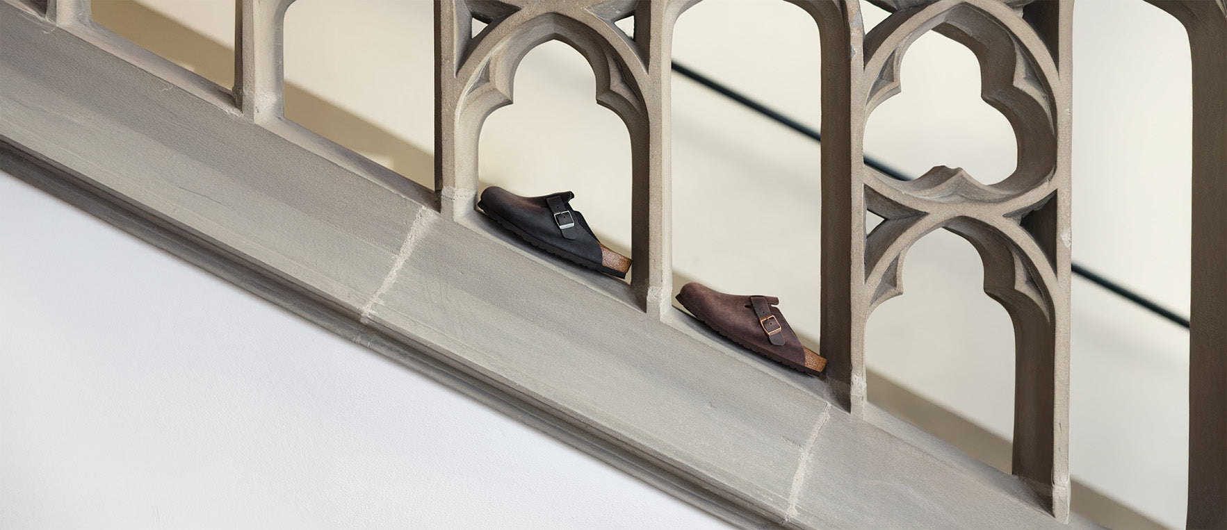 Primo piano di Birkenstock Boston Sabot Unisex, una black e una habana appoggiarte su un muretto 