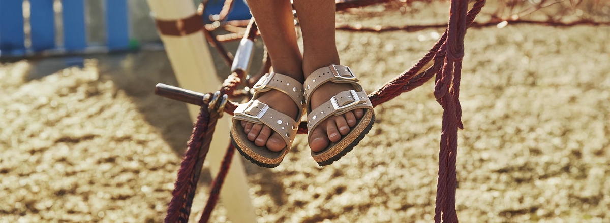 primo piano frontale di sandali birkenstock arizona bambino con borchie indossate da bambina che si trova su un gioco