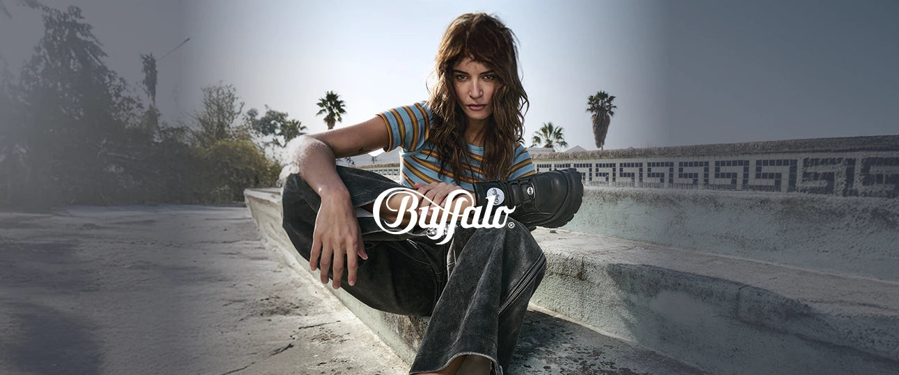 Donna seduta su scalini di cemento con una gamba appoggiata su ginocchio e indosso scarpe 1339-14 2.0 nere di buffalo