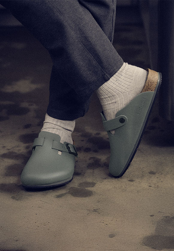 Scarpe professionali Birkenstock Boston Pro verdi thyme indossate con calzini bianchi e pantaloni grigi, su pavimento industriale – calzature comode per settore horeca, hotel, mense e ristoranti.
