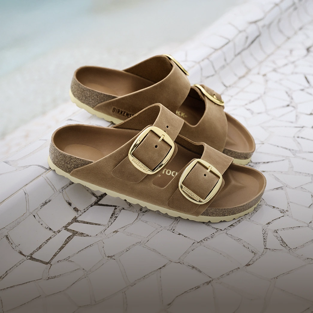 primo piano di sandali arizona big buckle birkenstock color cognac appoggiate su pavimentazione in pietra bianca