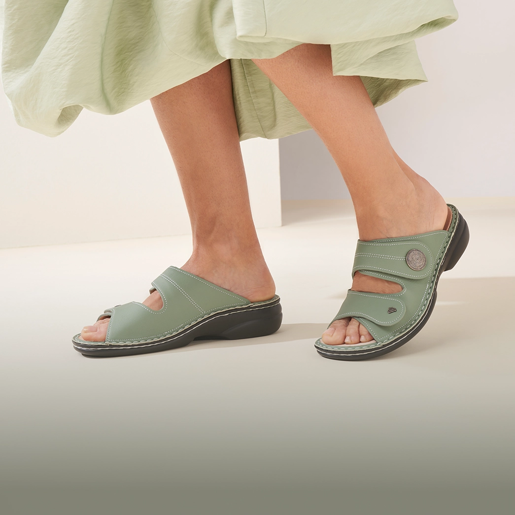 primo piano laterale di piedi di donna che indossa ciabatte finncomfort sansibar verdi 
