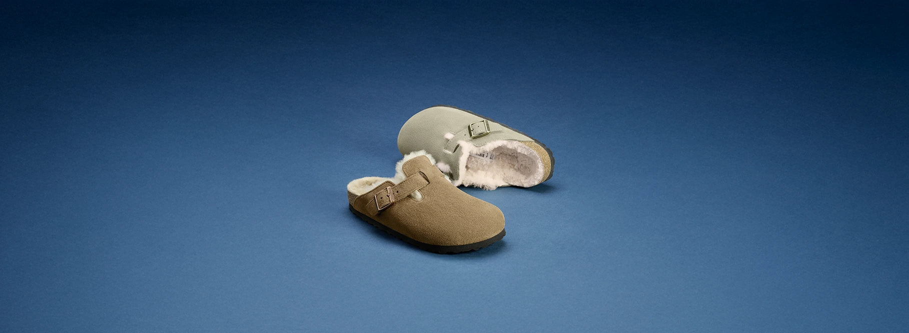 Primo piano laterale di boston sabot birkenstock con pelo, uno taupe e uno marrone, su sfondo blu
