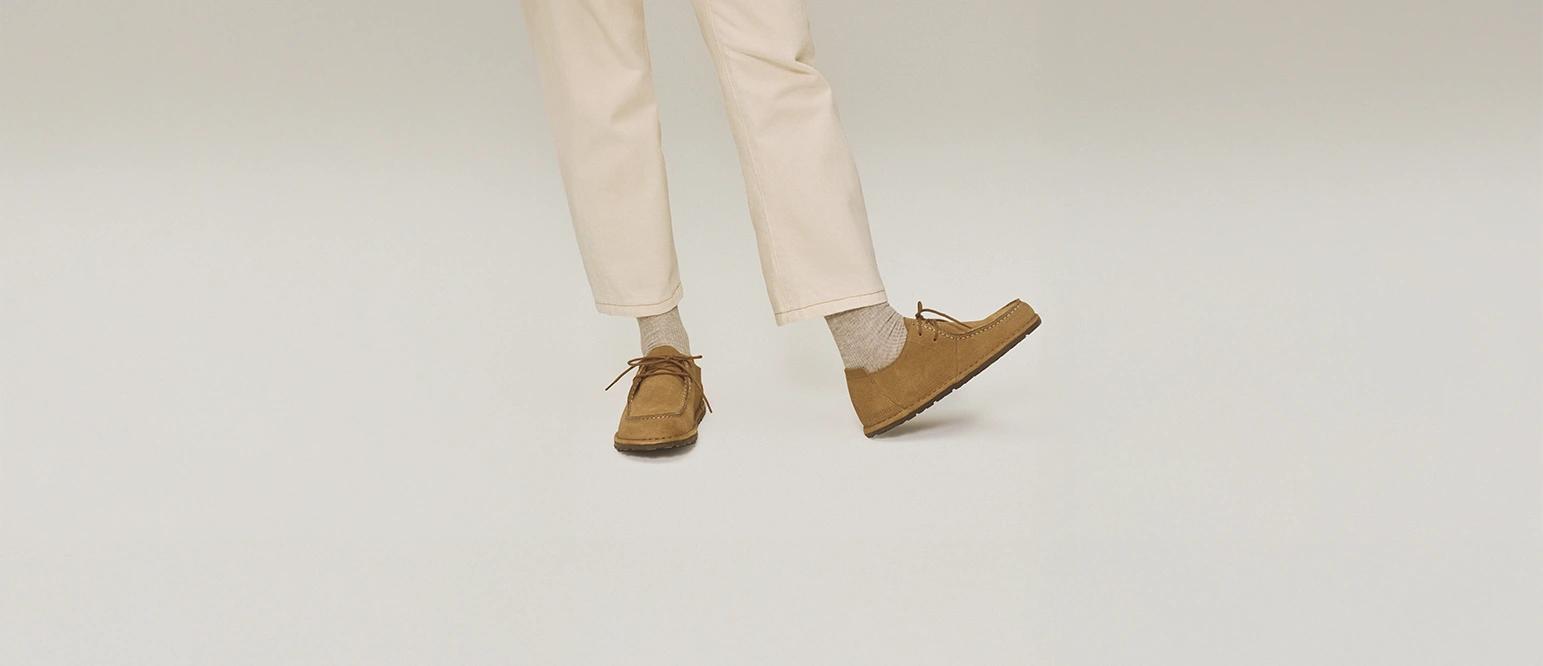 primo piano di scarpe mocassino utti indossate da persona in piedi con pantaloni chiari e calze beige