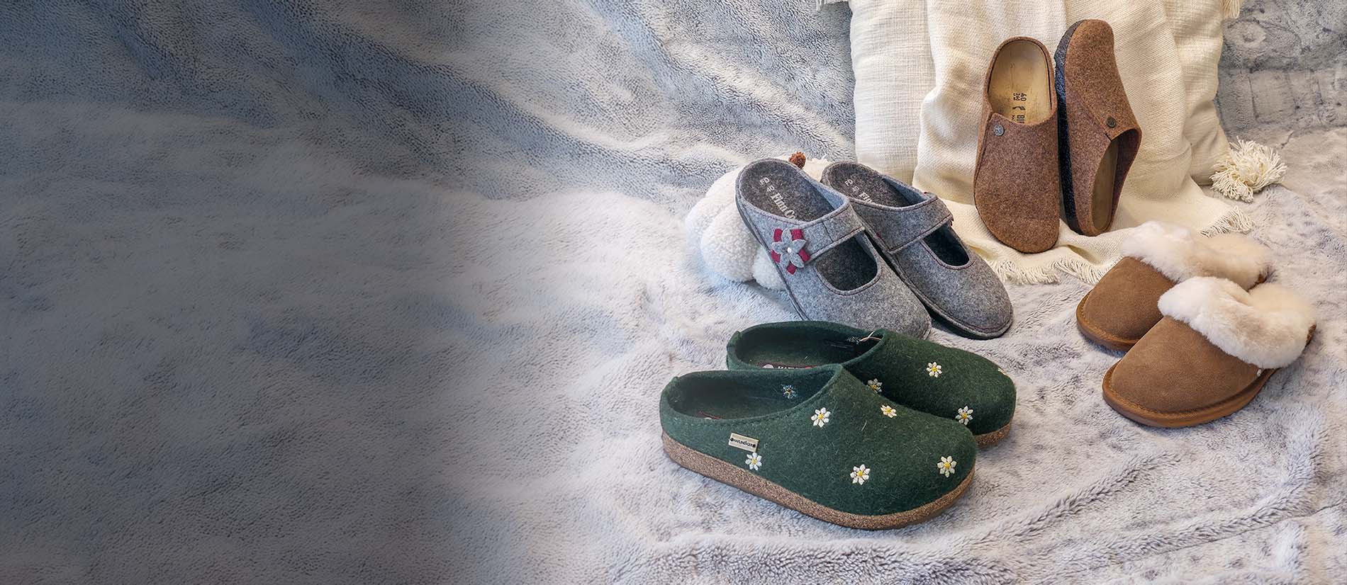 Primo piano di Pantofole invernali di birkenstock, haflinger, finncomfort, emu_australia appoggiate su un plaid bianco