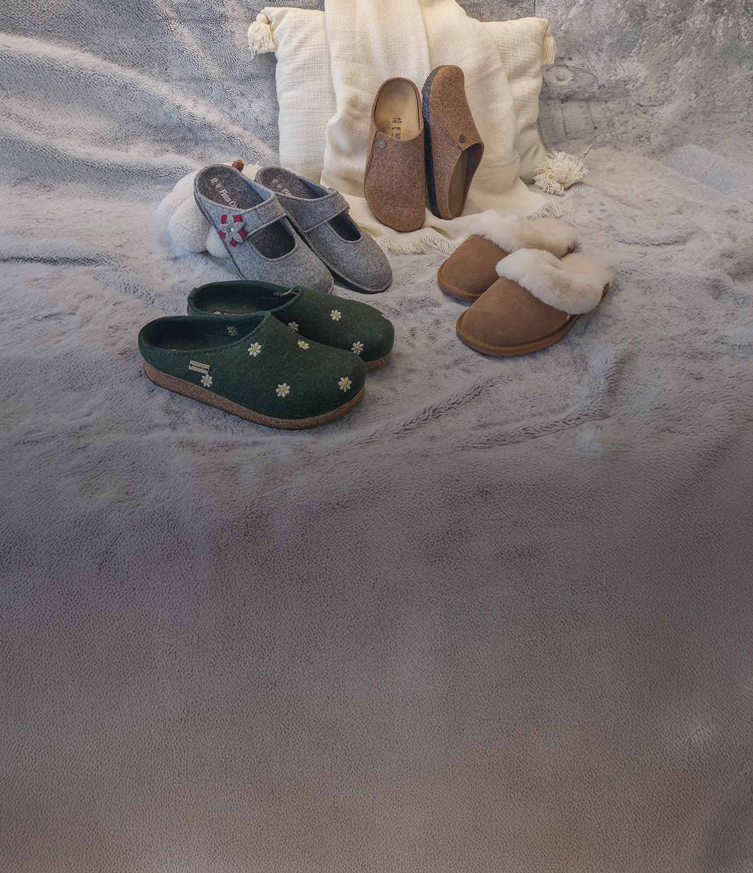 Primo piano di Pantofole invernali di haflinger, emu australia, birkenstock, , finncomfort appoggiate su un plaid bianco