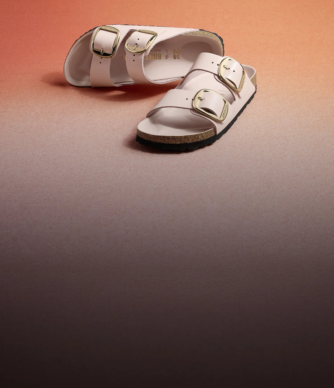 Primo piano su sfondo gradiente arancione rosa di sandali arizona birkenstock big buckle shine ecru