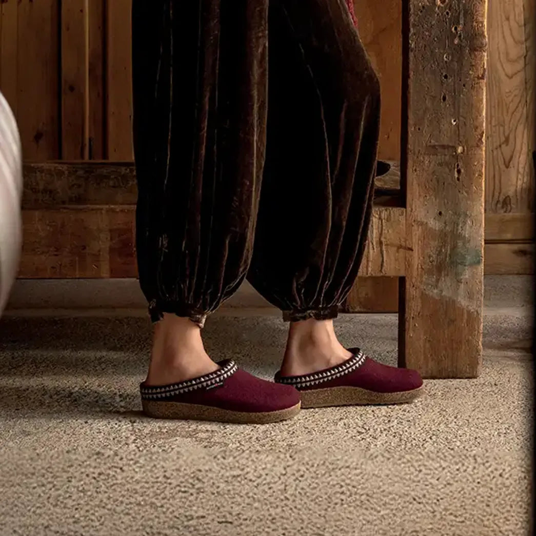 primo piano laterale di sabot haflinger pantofole in lana modello lucky color bordeaux indossate da donna con pantaoloni marroni