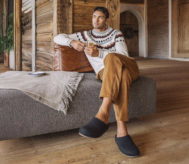 Uomo con indosso pantofole haflinger Soft Sabot Unisex jeans seduto su un divano in una baita