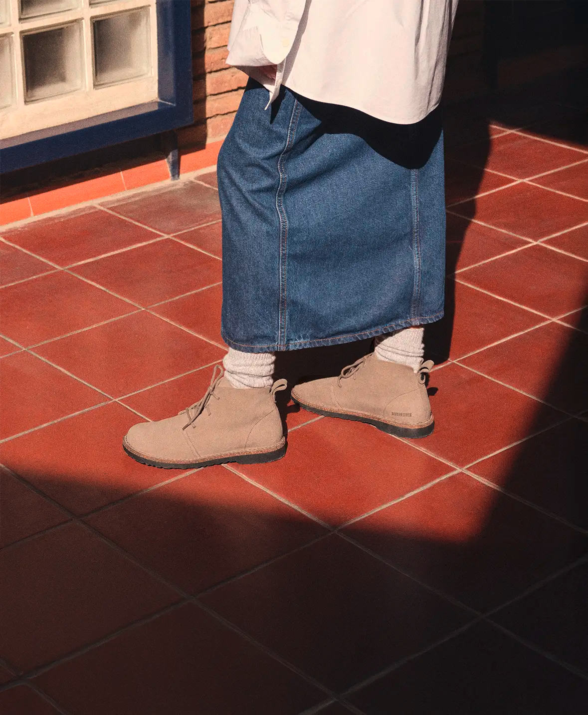 Primo piano di birkenstock stivaletti uppsala indossati da una donna con gonna di jeans lunga su mattonelle rosse