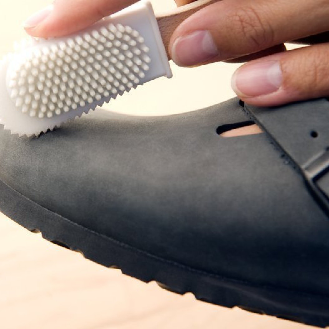 Primo piano della pulizia del Birkenstock Boston Sabot Unisex in pelle ingrassata nera, con spazzolino a setole in nylon per rimuovere delicatamente segni e macchie sulla tomaia.