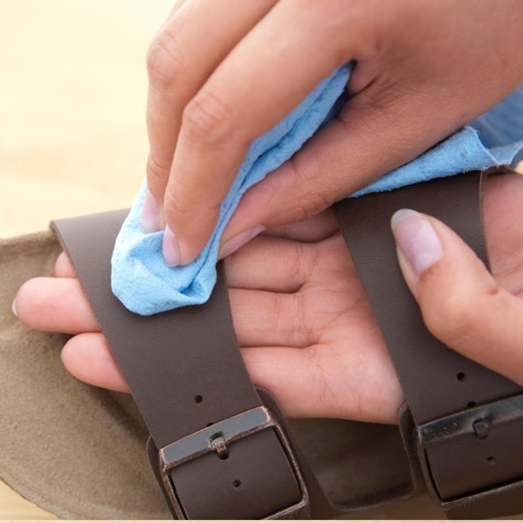 Primo piano della pulizia del sandalo Birkenstock Arizona marrone con tomaia in Birko-Flor, utilizzando un panno umido in microfibra azzurro.