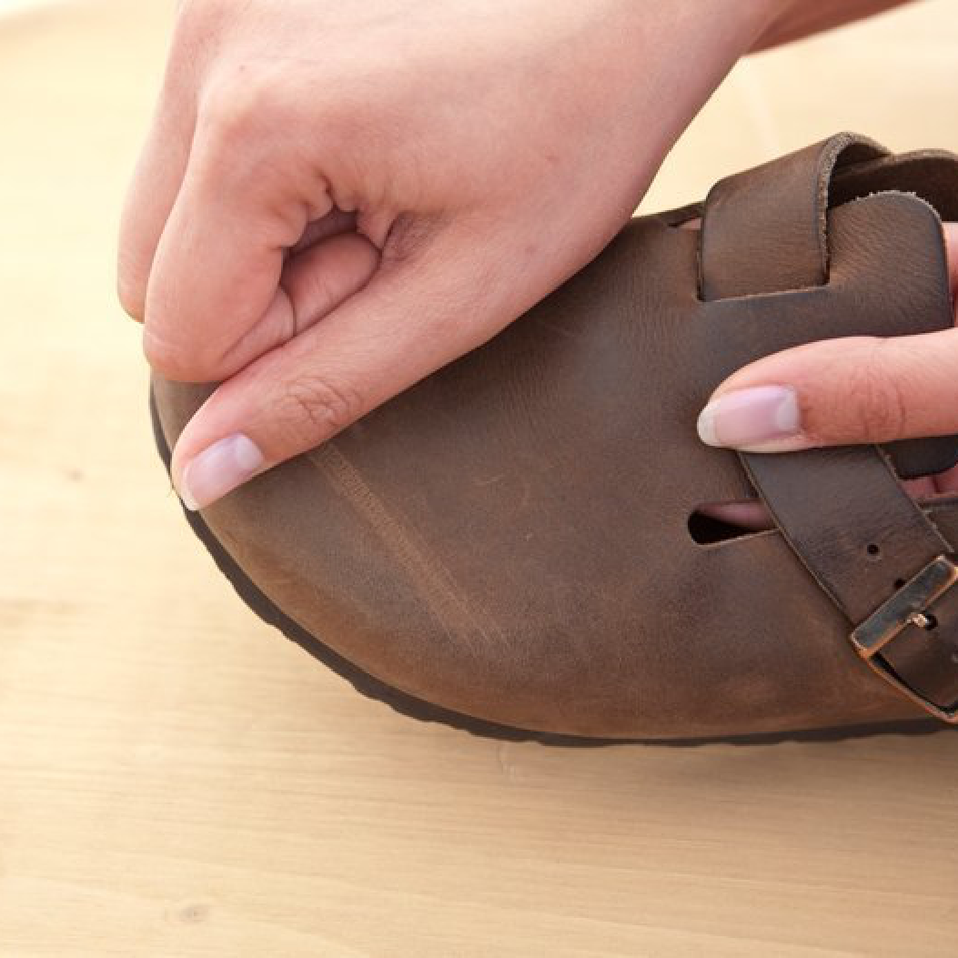 Primo piano di una mano che strofina delicatamente la tomaia in pelle naturale del Birkenstock Boston Sabot Unisex marrone per rimuovere piccoli graffi.