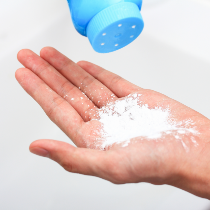 Primo piano di una mano con talco bianco per la pulizia versato da un contenitore azzurro, su sfondo bianco.